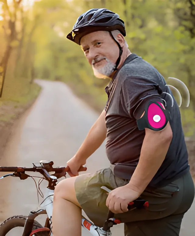 Actieve senior met fietshelm fietst op een zonnig bospad met een roze SOS-Knop op zijn bovenarm